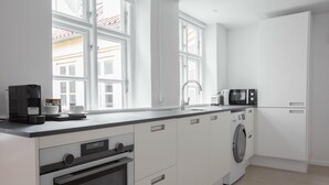 A modern kitchen with white cabinets, a built-in oven, a washing machine, a microwave, and a coffee maker. - Beautiful 2-bed in top Copenhagen Location (Copenhagen)