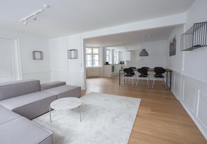 Un salon moderne avec un canapé gris, une table basse ronde et une cuisine en arrière-plan.
