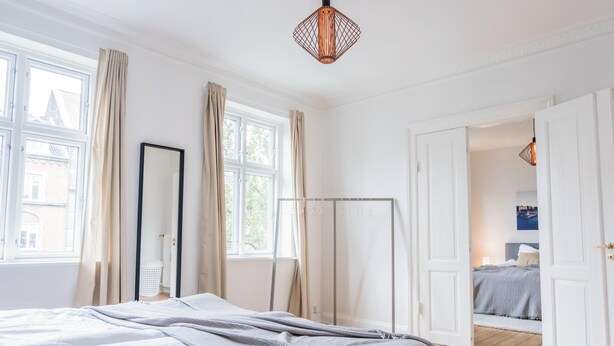 Un dormitorio con cama, armario, espejo y puerta que da a otra habitación.