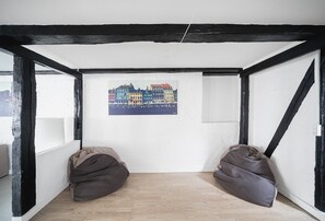 A room with exposed black beams, a white wall, and a wooden floor. There are two bean bags and a framed picture of a colorful building. - Charming 2-bed Duplex in Great Location (Copenhagen)