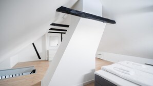 A modern, minimalist bedroom with a sloped ceiling, a bed with white bedding, and a wooden floor. - Charming 2-bed Duplex in Great Location (Copenhagen)