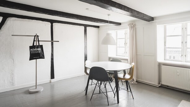 A modern dining area with a round table, black chairs, a hanging pendant light, and a flag on a stand. - Charming 2-bed Duplex in Great Location (Copenhagen)