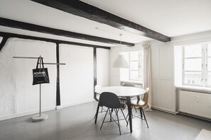 Un espace repas moderne avec une table ronde, des chaises noires, un luminaire suspendu et un drapeau sur un présentoir.