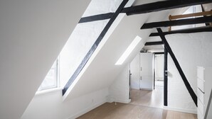 An attic bedroom with slanted ceilings, exposed beams, and a view into another room. - Charming 2-bed Duplex in Great Location (Copenhagen)