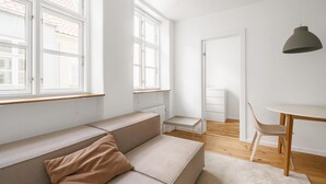 Un salón minimalista con un sofá color beige, una mesita y una silla. Amplias ventanas ofrecen luz natural y vistas al exterior.