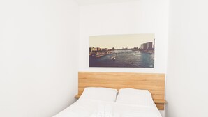 Habitación de hotel con cama, ropa de cama blanca, cabecera de madera y vistas de la ciudad en la pared.