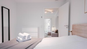 A modern hotel room with a large bed, a wooden headboard, and a view of the city through the window. - Stunning 2-bed w Large Balcony (Copenhagen)