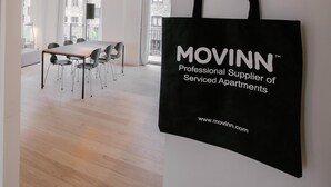 A modern interior with a dining area, a hanging black bag with text, and a view of buildings outside. - Stunning 2-bed w Large Balcony (Copenhagen)