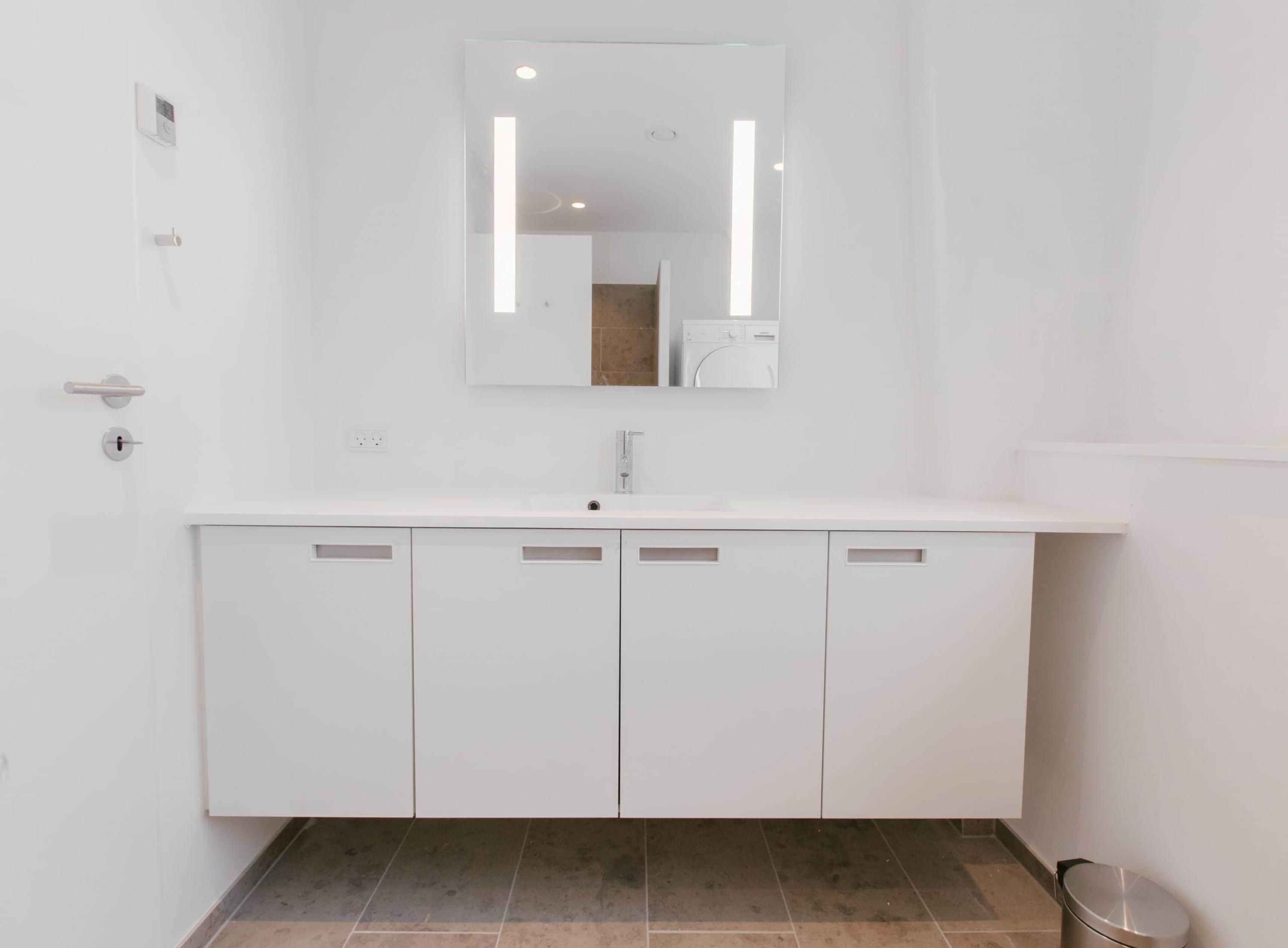 A modern bathroom with a white vanity, a mirror, and a tiled floor.