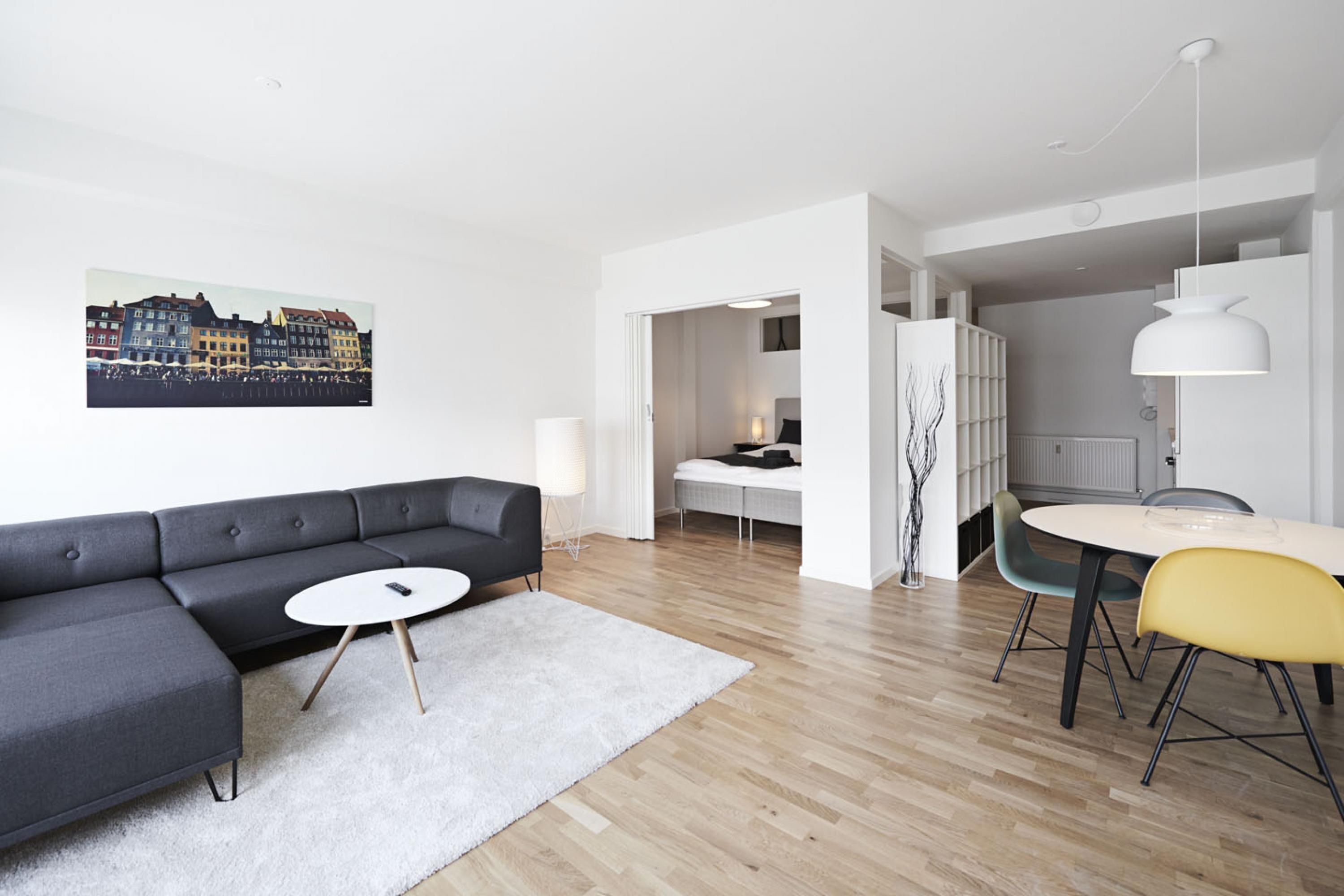 A modern living room with a gray sectional sofa, a round coffee table, and a dining area with a white table and chairs.