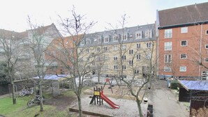 Ein Spielplatz mit Rutsche und Schaukeln, umgeben von Bäumen und Gebäuden.