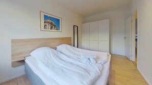 Ein Schlafzimmer mit einem Bett, einem hölzernen Kopfende, einem Kleiderschrank und einem gerahmten Bild an der Wand.
