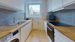 A compact kitchen with wooden countertops, a built-in washing machine, and a window with a view of buildings outside. - Fantastic 2-bed in Frederiksberg C (Frederiksberg)