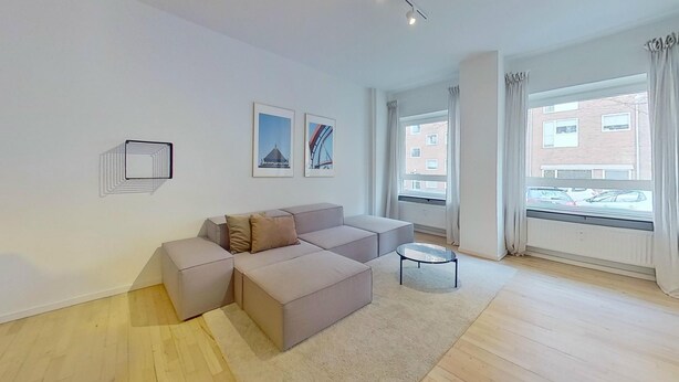 Ein modernes Wohnzimmer mit einer Eckcouch, einem kleinen runden Tisch und großen Fenstern mit Blick auf die Stadt.