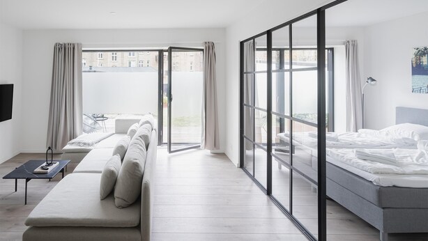 A modern hotel room with a sofa, a bed, and a balcony with a view of buildings. - Fantastic 1-bed Apartment w Private Terrace (Aarhus)