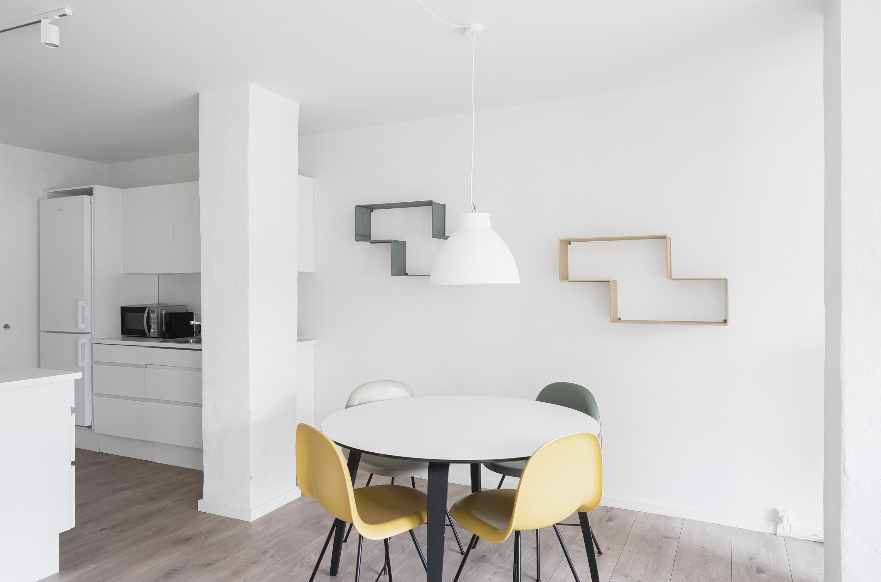 Una cocina moderna con armarios blancos, un microondas y un comedor con una mesa redonda y sillas amarillas.