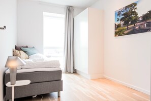 A modern bedroom with a bed, a bedside table with a lamp, a window with curtains, and a wall-mounted picture. - Modern 3-bed Apartment in Nordhavn (Copenhagen)