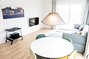 A modern living room with a round dining table, a grey sofa, a floor lamp, and a TV mounted on the wall. - Modern 3-bed Apartment in Nordhavn (Copenhagen)
