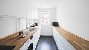 Une cuisine étroite avec des meubles blancs, un plan de travail en bois, un évier et une fenêtre.