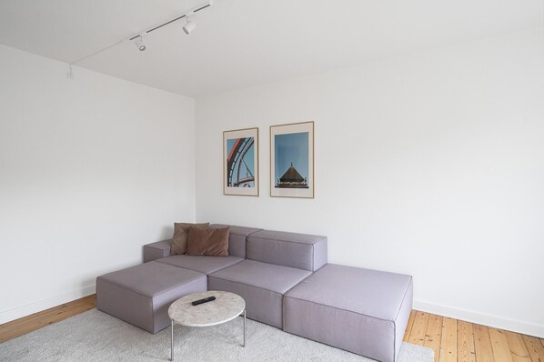 A modern living room with a grey sectional sofa, a round coffee table, and two framed pictures on the wall.