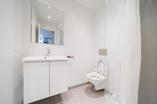 Un baño moderno con un lavamanos, espejo y retrete blancos.