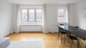 Une pièce dotée d’une grande fenêtre, d’un plancher en bois et d’une table noire avec des chaises.