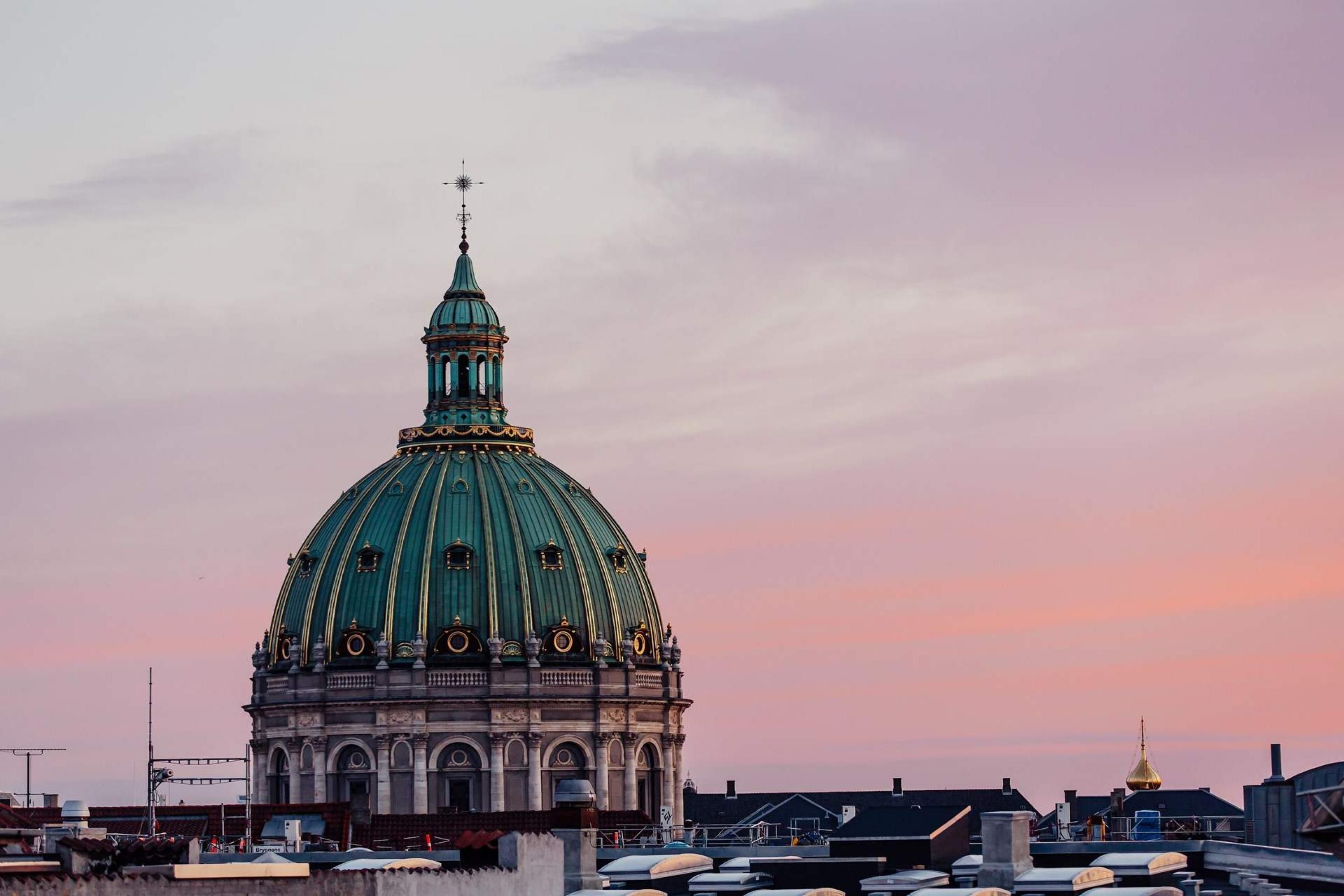 A large domed building with a spire, surrounded by rooftops and other structures.