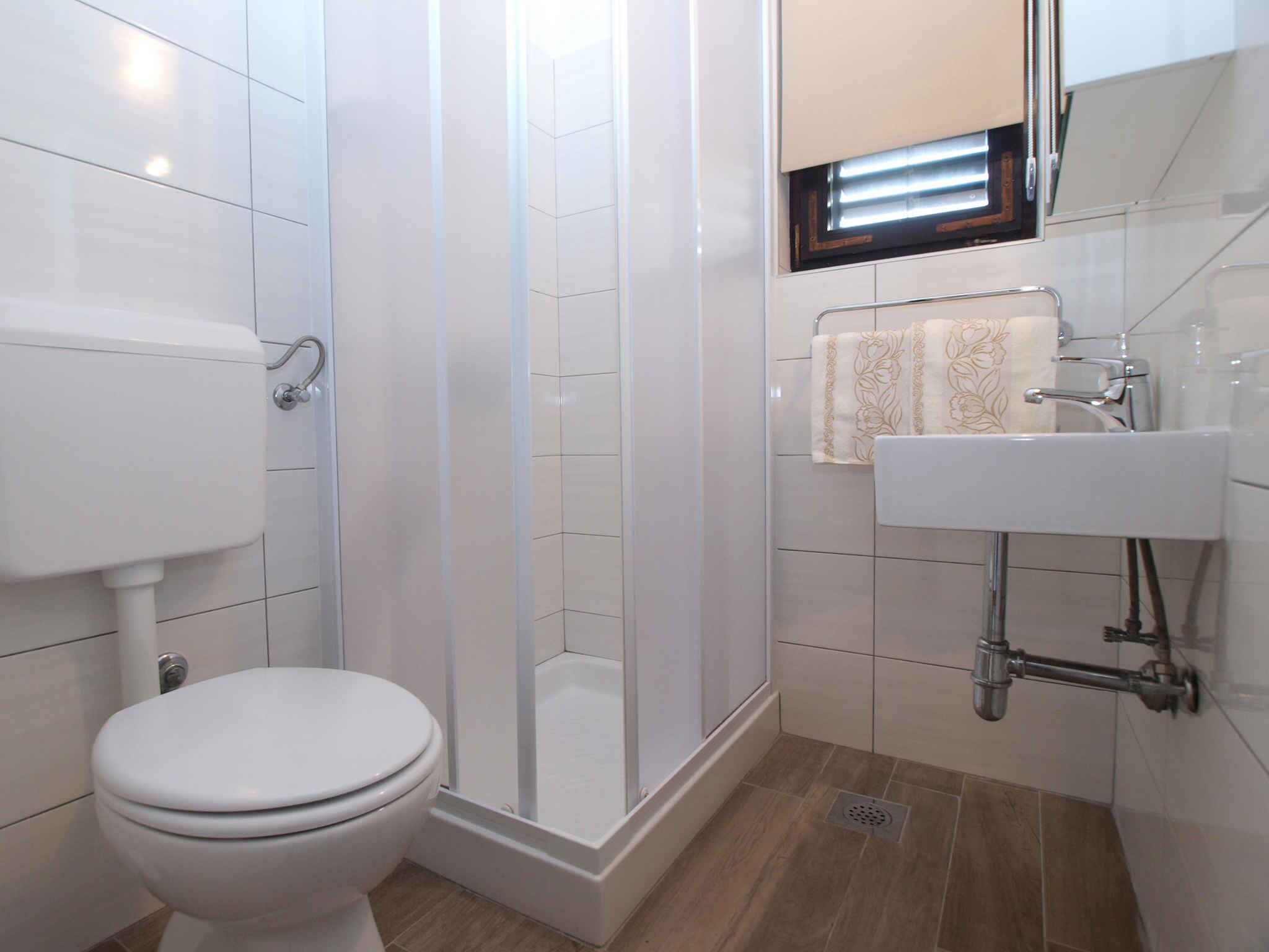A bathroom with a toilet, a glass-enclosed shower, and a sink with a towel hanging above it.