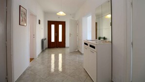 A hallway with a tiled floor, a wooden door, a white cabinet, and a pendant light.
