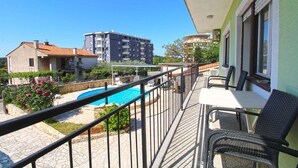 A balcony with a pool, outdoor seating, and a view of surrounding buildings.