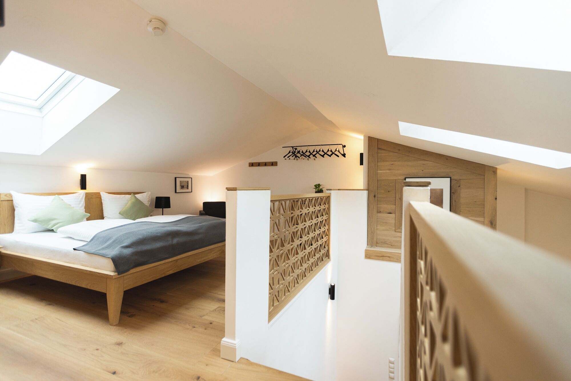 A modern, well-lit attic bedroom with a skylight, a bed with a wooden headboard, a small seating area, and a wooden wall panel.