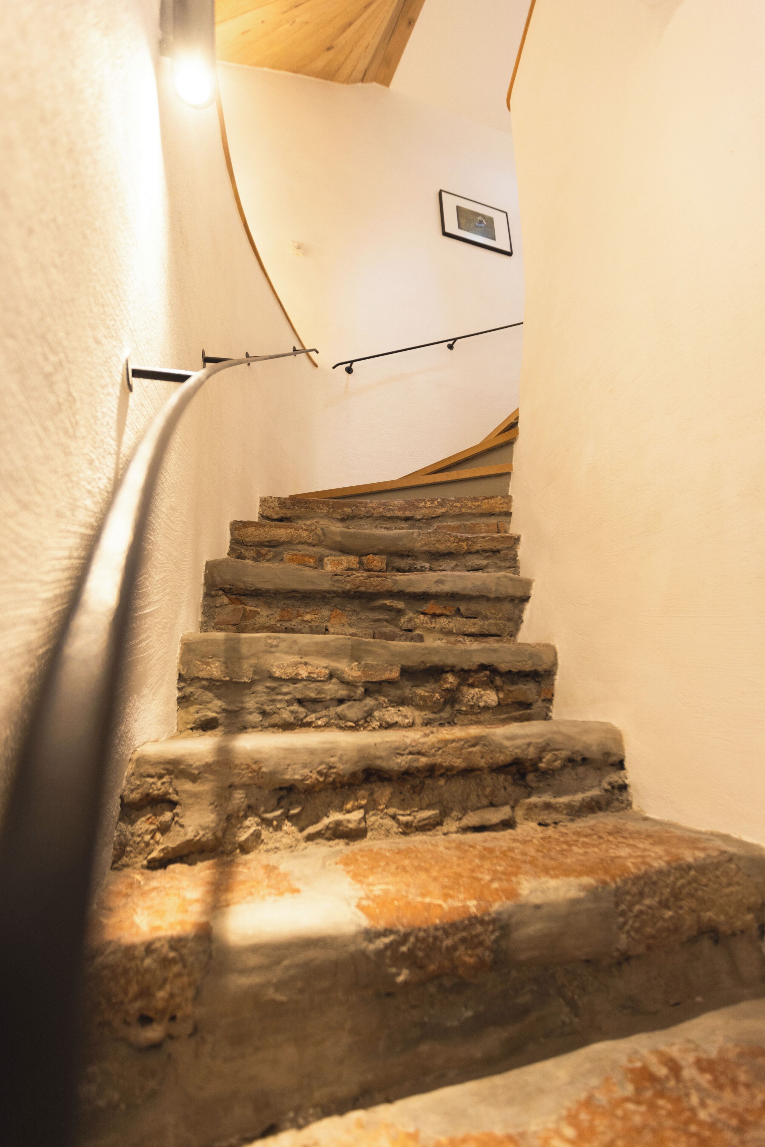 A stone staircase with a wooden handrail, leading up to a landing with a framed picture.