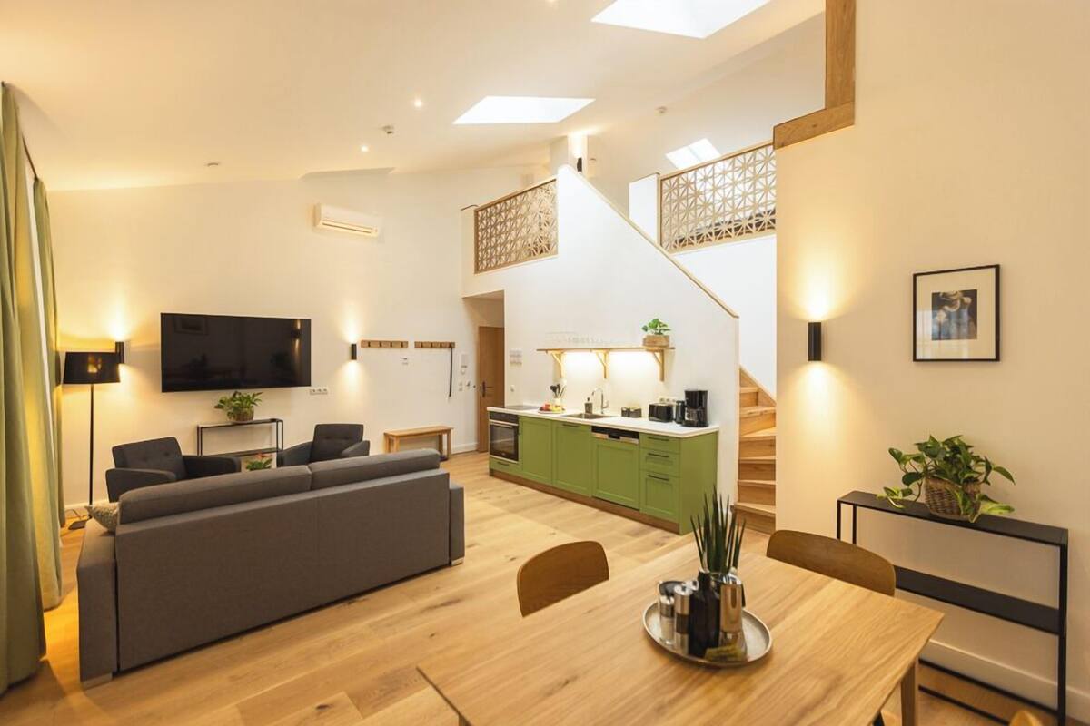 Een modern appartement met een woonkamer, eethoek, keuken en trap.