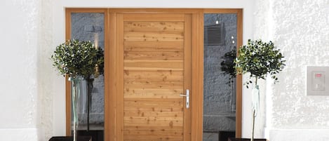A building entrance with a wooden door, two potted plants, and a sign above the door.