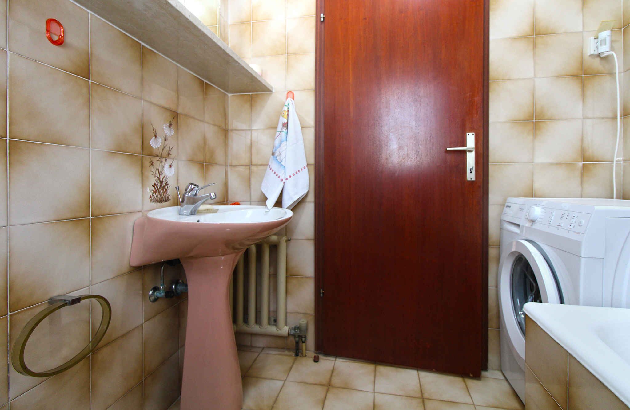 Une salle de bain avec un lavabo rose, une porte en bois et un lave-linge.