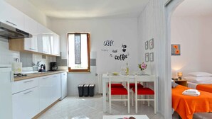 A compact hotel room with a kitchenette, a dining area with a table and chairs, and a bed with an orange bedspread. - Holiday apartment with garden and barbecue (Fažana)