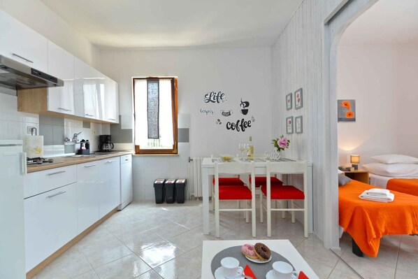 A compact hotel room with a kitchenette, a dining area with a table and chairs, and a bed with an orange bedspread. - Holiday apartment with garden and barbecue (Fažana)