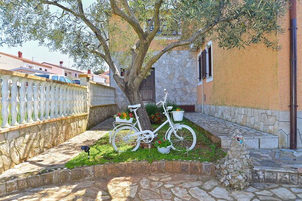 Uma bicicleta branca estacionada perto de uma árvore em um pátio com muro de pedra e cerca branca.
