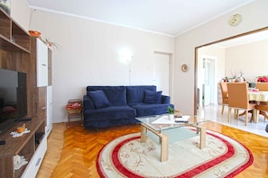 A living room with a blue sofa, a glass coffee table, a wooden TV stand, and a red and white patterned rug. - Holiday apartment with air conditioning (Pula)