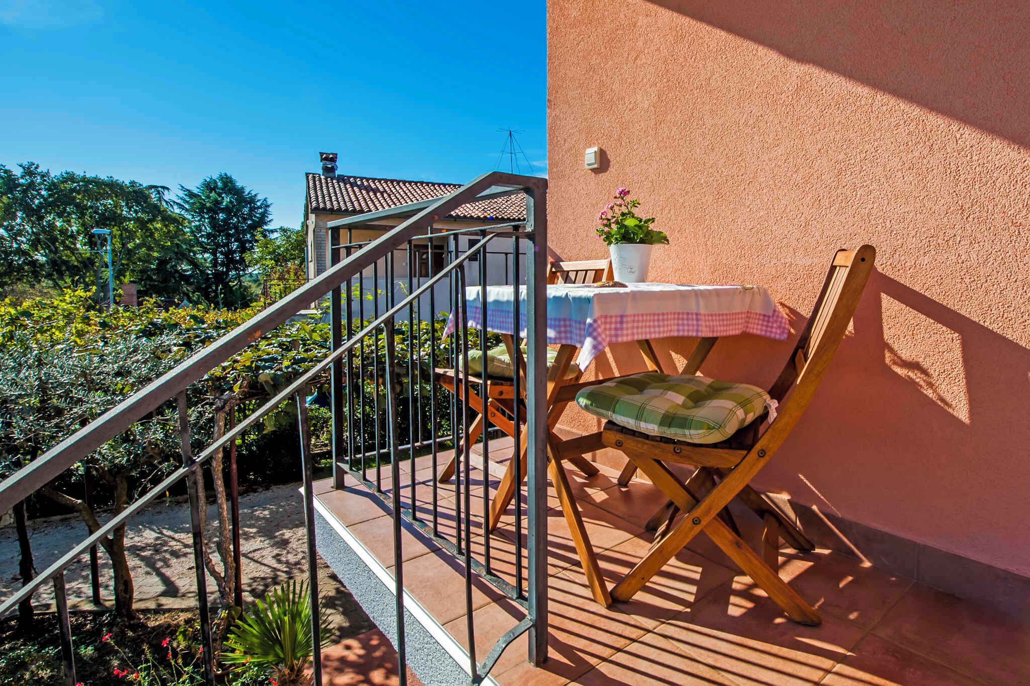 Ein Balkon mit Holzstuhl und Tisch, eine Treppe und ein Gebäude mit einem Ziegeldach im Hintergrund.