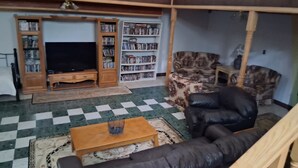 Una sala de estar con piso a cuadros, un televisor, una estantería, un sillón estampado y un sofá de cuero.
