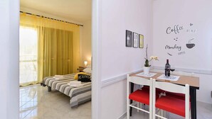A hotel room with a bed, a desk, and a chair. There is a window with curtains, a wall with a coffee-themed decoration, and a small table with a vase and a bottle. - Holiday apartment with garden and barbecue (Fažana)
