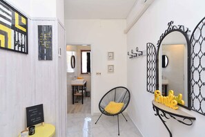 Un pasillo con una silla negra, un cojín amarillo y un espejo con marco decorativo.