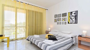 A hotel room with a bed, a desk, a chair, and a balcony with yellow curtains. - Holiday apartment with garden and barbecue (Fažana)