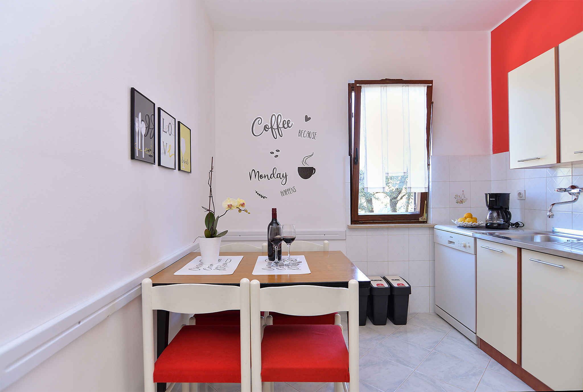 A small kitchen with a dining table, chairs, and a window. There are framed pictures on the wall and a coffee sign.