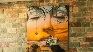 Dos mujeres en una piscina con un muro de piedra y un atardecer pintado en el fondo.