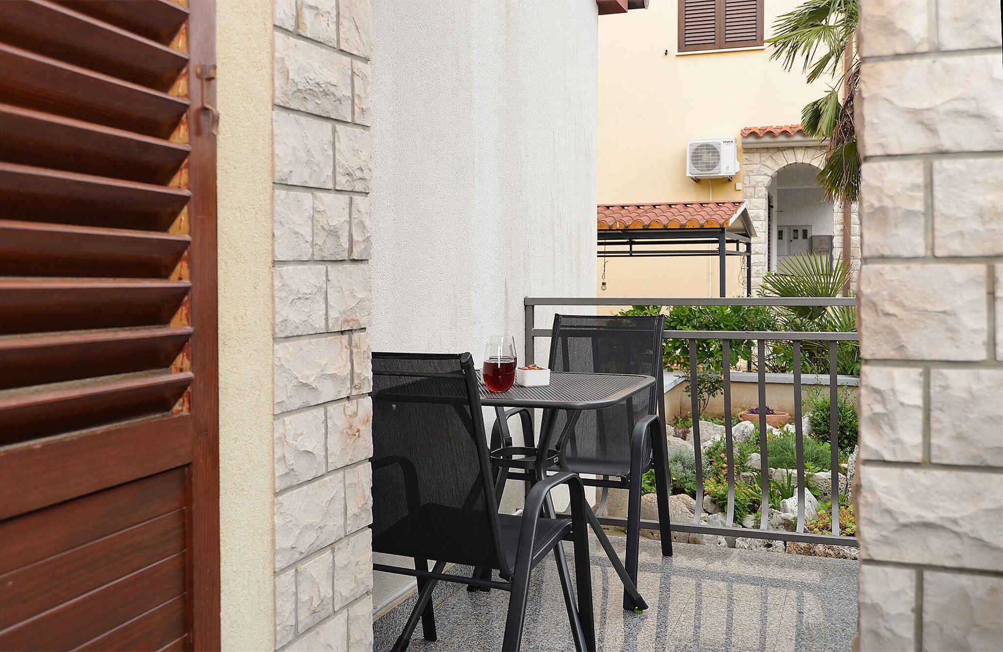 An outdoor seating area with two black chairs and a table, a stone wall, and a view of a building with a tiled roof.