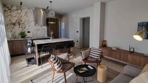 Una sala moderna con sofá, sillones, una mesa de centro y una zona de comedor con cocina al fondo.