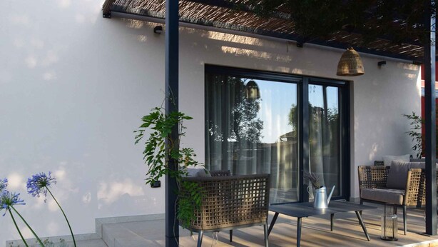 Un patio exterior con muebles de mimbre, una mesa de vidrio y una lámpara de metal.