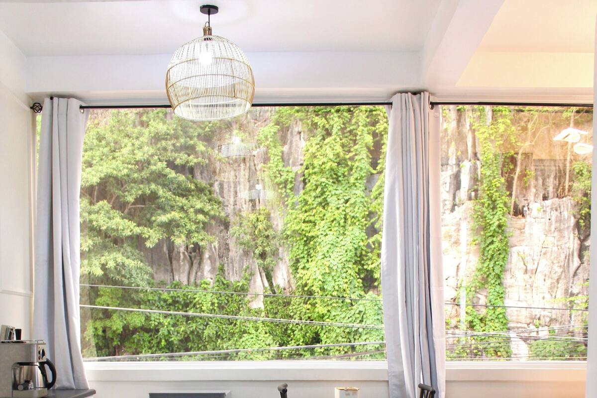 A bedroom with a large bed, a small table, and a view of greenery outside.